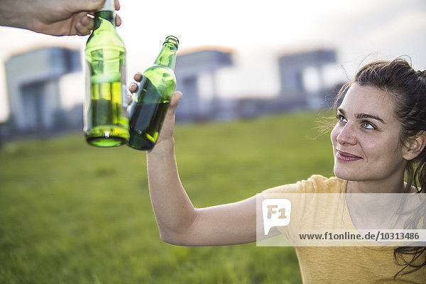Deutschland  Köln  Frauentoast mit Bierflasche auf einer Wiese bei Abenddämmerung