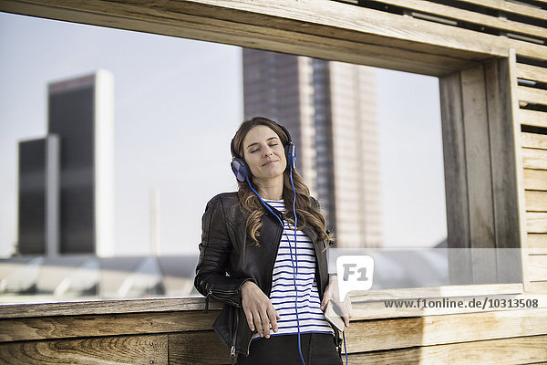 Germany  Frankfurt  young woman with closed eyes hearing music with headphones