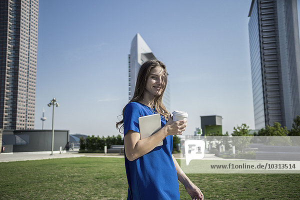 Deutschland  Frankfurt  lächelnde Frau mit Kaffee zum Mitnehmen und Mini-Tablette