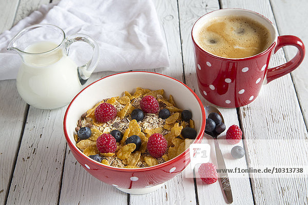 Schale Müsli mit frischen Früchten  Tasse Kaffee und Milchkännchen auf weißem Holz
