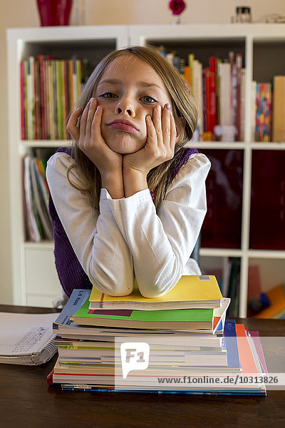 Portrait of unhappy girl leaning on stack of school books