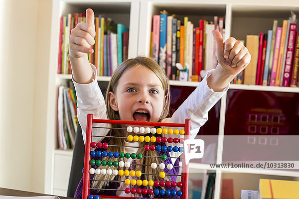 Portrait of cheering girl sitting behind abacus showing thumbs up