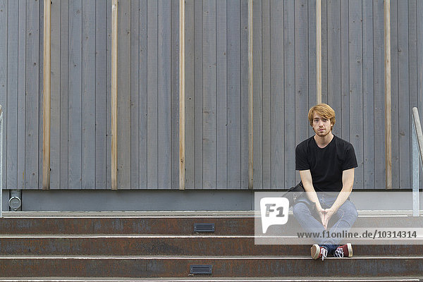Junger Mann auf einer Treppe vor der Holzfassade sitzend