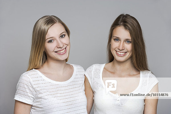 Portrait of two smiling young women in front of grey background