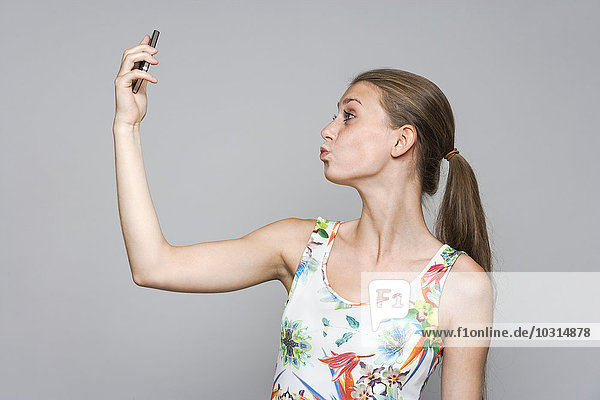 Junge Frau  die einen Selfie mit Smartphone vor grauem Hintergrund nimmt.