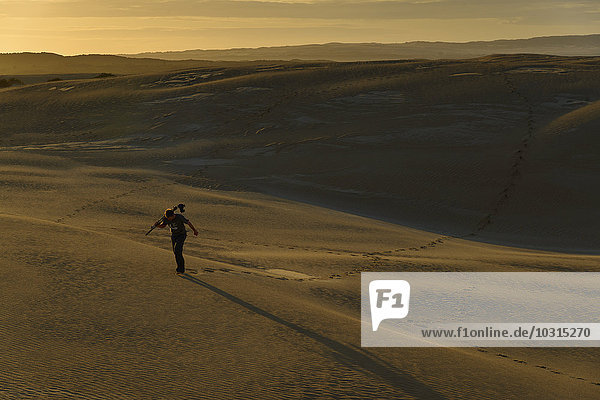 Südaustralien Mann mit Stativ und Kamera bei Dämmerung durch Sanddünen gehend