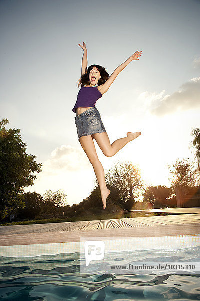 Exuberant young woman jumping at the poolside