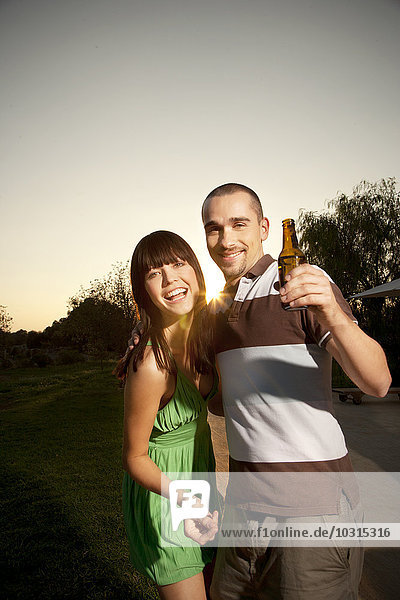 Glückliches junges Paar mit Bierflasche bei Sonnenuntergang