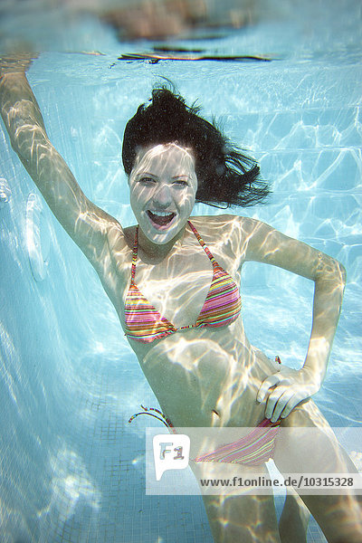 Porträt der lachenden jungen Frau unter Wasser im Schwimmbad