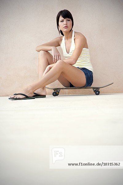 Porträt einer jungen Frau  die auf ihrem Longboard sitzt.