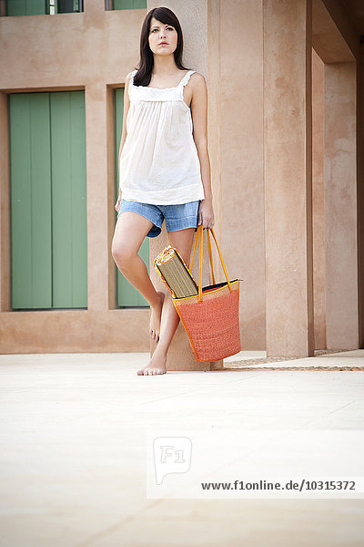 Young woman with bag and beach mat leaning against pillar