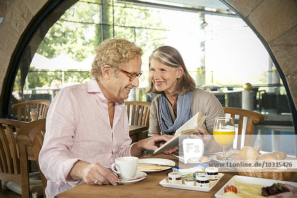 Lächelndes Seniorenpaar beim Lesen und Frühstücken im Café
