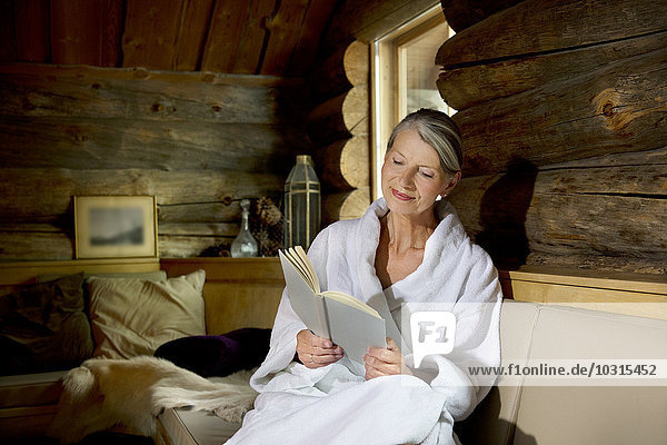 Smiling senior woman sitting on bench in bathrobe reading a book