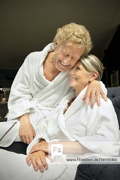 Glückliches Seniorenpaar im Bademantel umarmt im Sessel