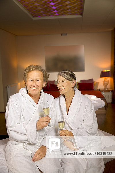 Smiling senior couple in bathrobes holding champagne glasses