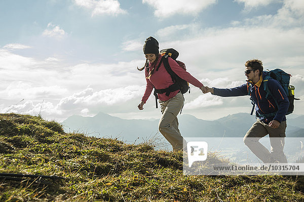 Austria  Tyrol  Tannheimer Tal  young couple hiking hand in hand on alpine meadow