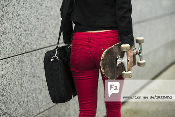 Junge Frau mit Tasche und Skateboard in roter Hose  Teilansicht
