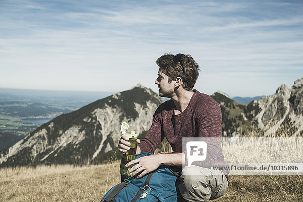 Austria  Tyrol  Tannheimer Tal  young man with backpack and drinking bottle on alpine meadow