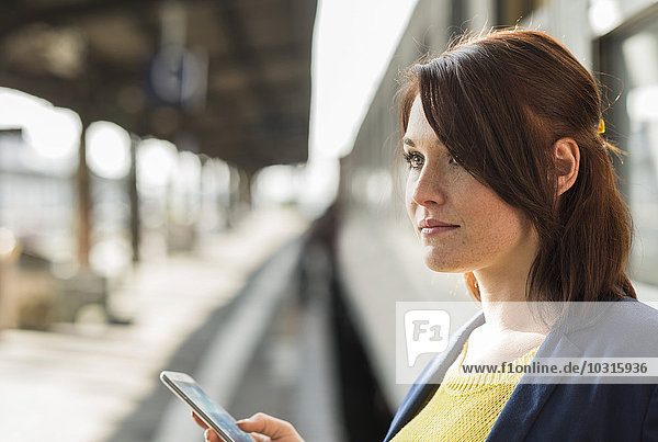 Junge Frau mit Handy am Bahnhof