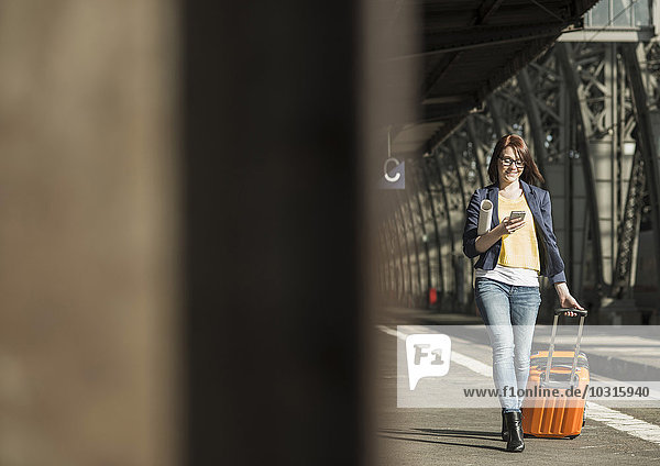 Young woman with cell phone and baggage at train station