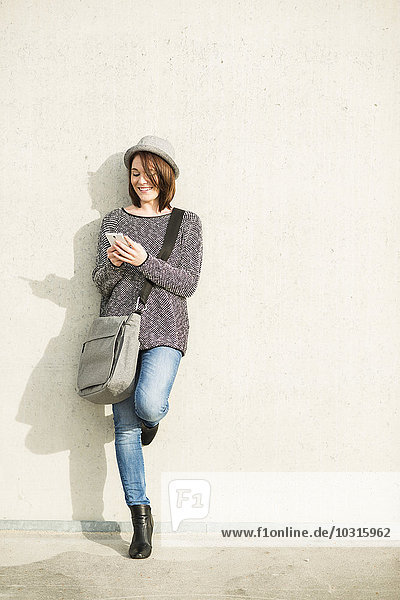 Lächelnde junge Frau mit Tasche und Handy