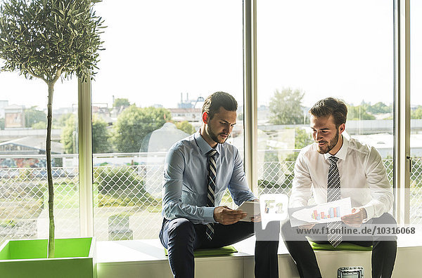 Two young businessmen looking at document and digital tablet
