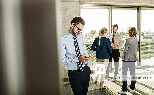 Businessman looking at smartphone with colleagues in background