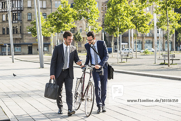 Zwei Geschäftsleute mit Fahrrad und Smartphone zu Fuß in der Stadt