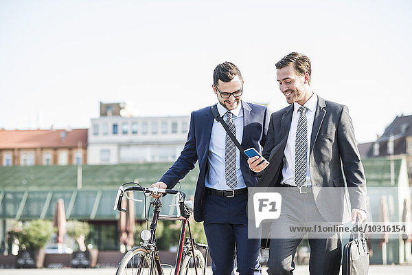 Zwei junge Geschäftsleute  die in der Stadt spazieren gehen und Fahrrad fahren.