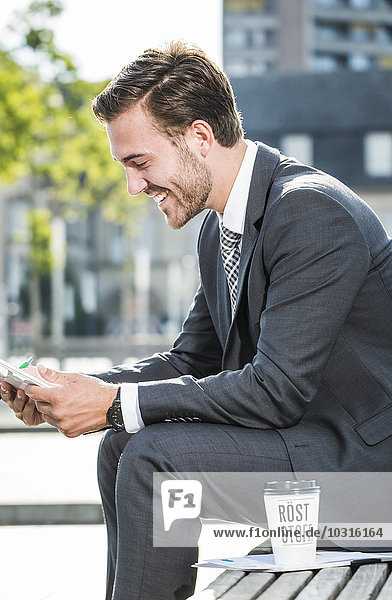 Ein junger Geschäftsmann sitzt auf einer Bank und benutzt ein digitales Tablett.
