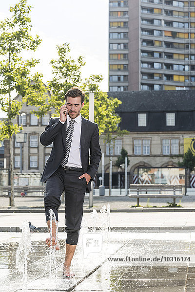 Young businessman standing in fountain  talking on the phone