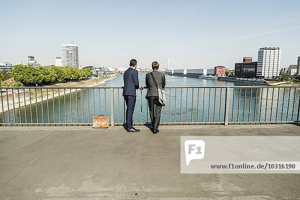 Junge Geschäftsleute stehen am Geländer und schauen auf den Fluss.