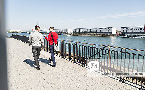 Two young businessmen walking by the riverside