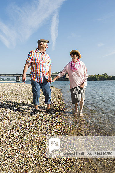 Germany  Ludwigshafen  happy senior couple walking hand in hand at riverside