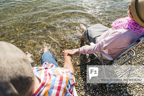 Seniorenpaar sitzt Hand in Hand auf Klappstühlen am Flussufer