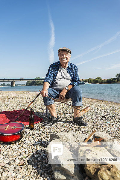 Germany  Ludwigshafen  portrait of smiling senior man barbecueing sausage on the beach
