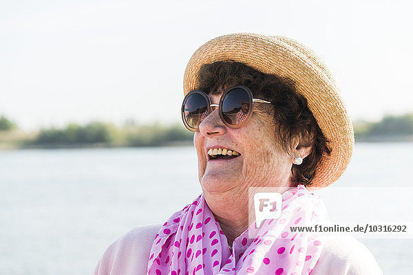 Porträt einer lächelnden Seniorin mit Sonnenbrille und Sommerhut