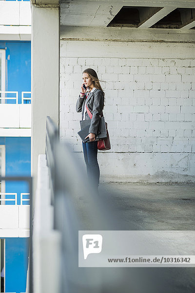 Junge Frau auf einem Parkplatz auf dem Handy mit Mappe