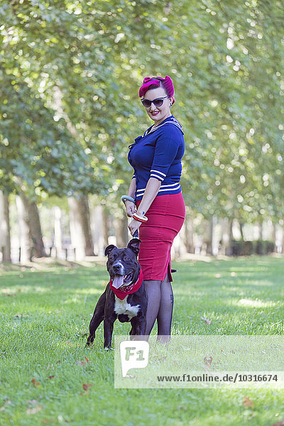 Porträt einer Frau mit gefärbtem Haar auf einer Wiese stehend mit ihrem Pitbull-Terrier