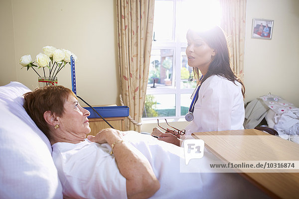 Seniorin im Krankenhausbett liegend im Gespräch mit dem Arzt