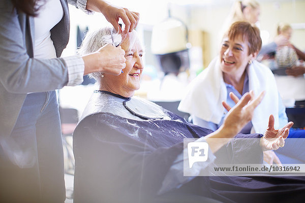 Female hairdresser cutting hair of senior woman