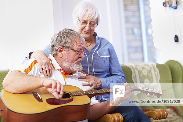Senior man with wife at home playing guitar