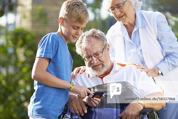 Großmutter und Enkel erklären Großvater im Rollstuhl Handy