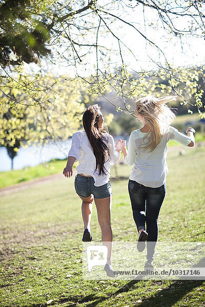Two female friends running together in a park