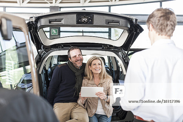 Smiling couple sitting in boot of new car at car dealership