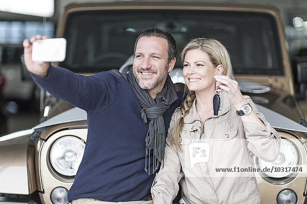 Glückliches Paar im Autohaus nimmt Selfie vor dem neuen Auto
