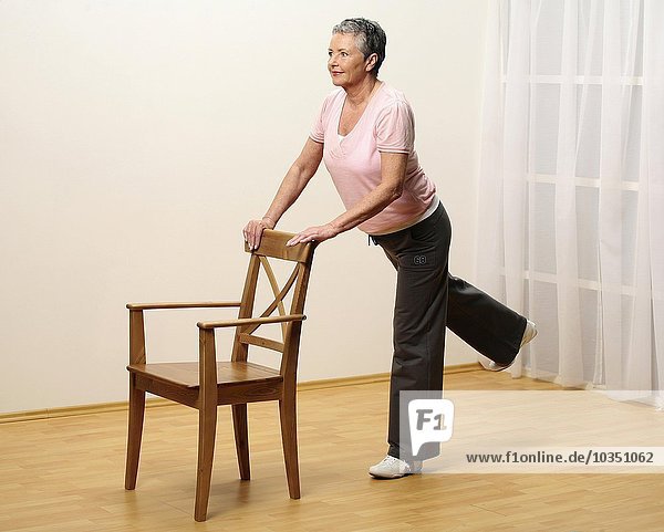 older woman doing gymnastics with a chair - sprawel leg to the back - muscularity - senior