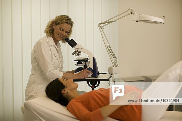 Arzt schaut durch ein Mikroskop neben einer schwangeren Patientin