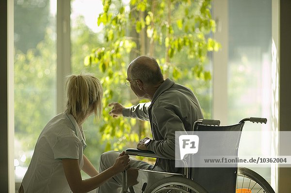 Krankenschwester und älterer Mann schauen aus dem Fenster