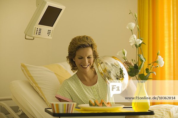 Frau im Krankenhausbett öffnet Essenstablett